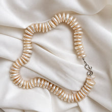 Load image into Gallery viewer, A strand of irregular cream-colored freshwater pearls arranged in a loop on draped white satin fabric, featuring a silver-tone clasp.
