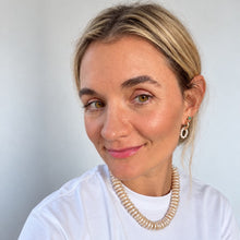 Load image into Gallery viewer, A woman with blonde hair pulled back, wearing a white t-shirt, a beige coiled pearl necklace, and gold hoop earrings, photographed against a light gray background.
